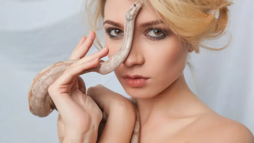 A woman holding a snake on her face to celebrate the Chinese New Year of the Snake, symbolizing strength and empowerment. Embrace self-care and empowerment with the Women's Personal Massager by Gaia in Love.