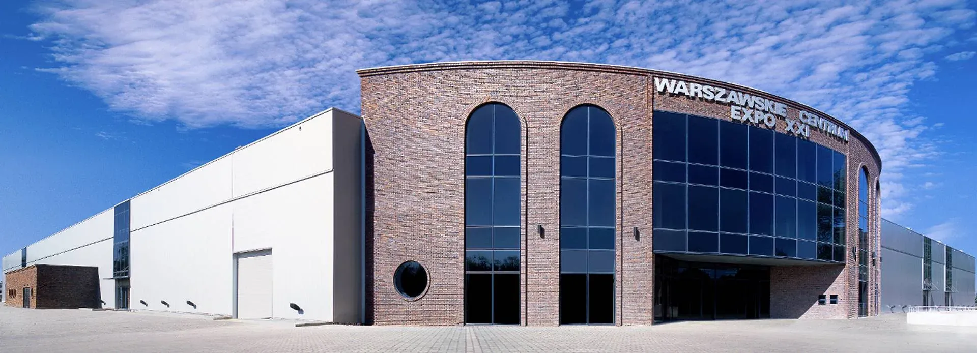A modern brick-and-glass exhibition center under a clear blue sky, serving as the official venue for EroChain Expo 2025.