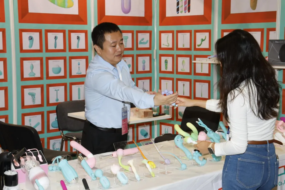 A vendor engaging with a visitor at an adult product booth during VENUS Berlin 2025.