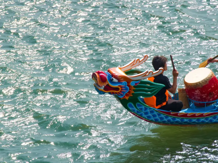 Dragon Boat Festival 2025 dragon boat race on sparkling river with drummer and paddlers in orange vests