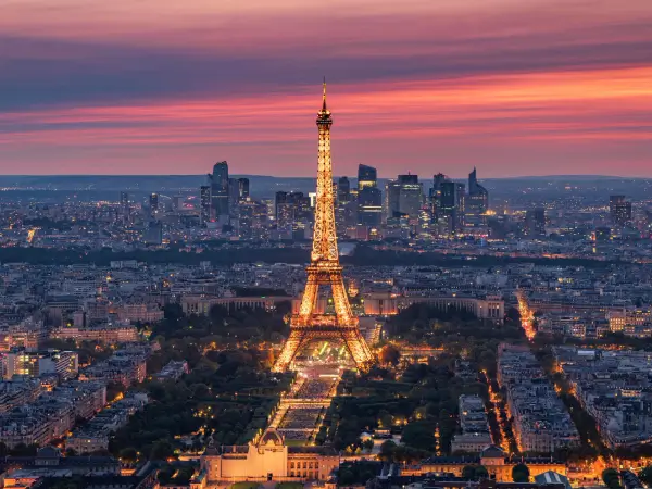 Vue panoramique de la tour Eiffel illuminée au crépuscule, dominant la ville de Paris sous un ciel coloré.