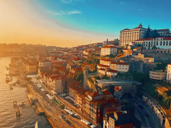 Vista panorâmica da cidade do Porto ao pôr do sol, com edifícios históricos e o rio Douro ao fundo.