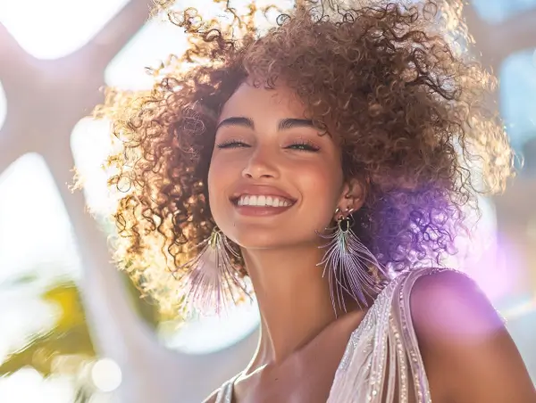 Mulher sorridente com cabelo cacheado sob a luz do sol, transmitindo alegria e confiança.