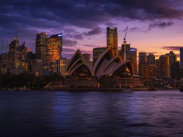 Sydney Opera House overlooking the harbour with the city skyline illuminated at sunset.