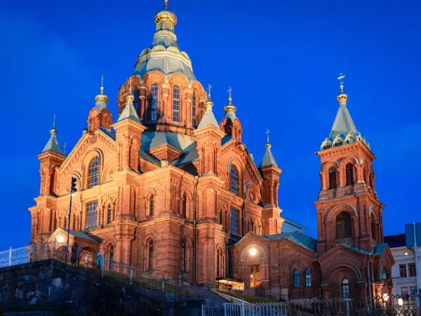 Helsingin Uspenskin katedraali iltahämärässä, valaistu kauniisti sinistä taivasta vasten.