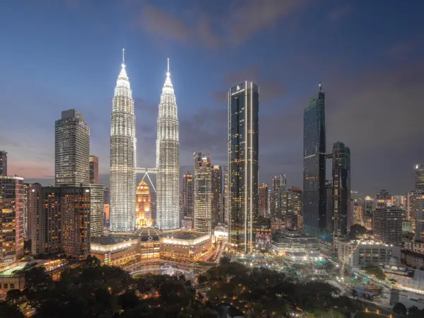 Pemandangan waktu senja Kuala Lumpur dengan Menara Berkembar Petronas yang bercahaya di tengah-tengah bandar dan bangunan pencakar langit moden di sekitarnya.