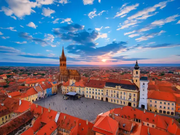 Piața Mare din Sibiu la apus, cu acoperișuri roșii și clădiri istorice văzute din aer.