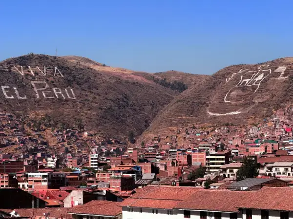 Vista panorámica de una ciudad andina del Perú con casas de ladrillo y colinas al fondo que forman el mensaje “Viva el Perú”.