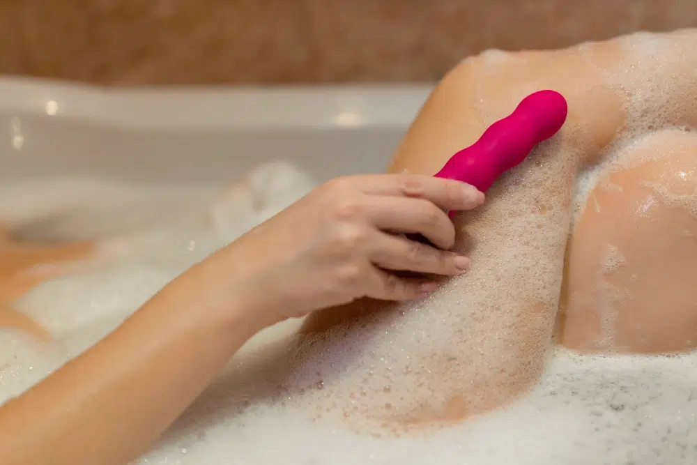 A person using a waterproof vibrator in a bathtub with foam, demonstrating the product's ability to handle water exposure.