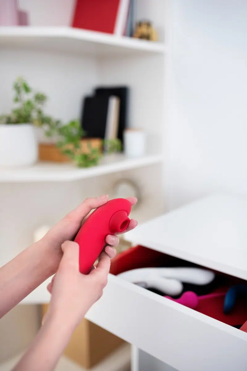 A person holding a red vibrator in a clean, minimal space, demonstrating how to properly handle and care for non-waterproof sex toys.
