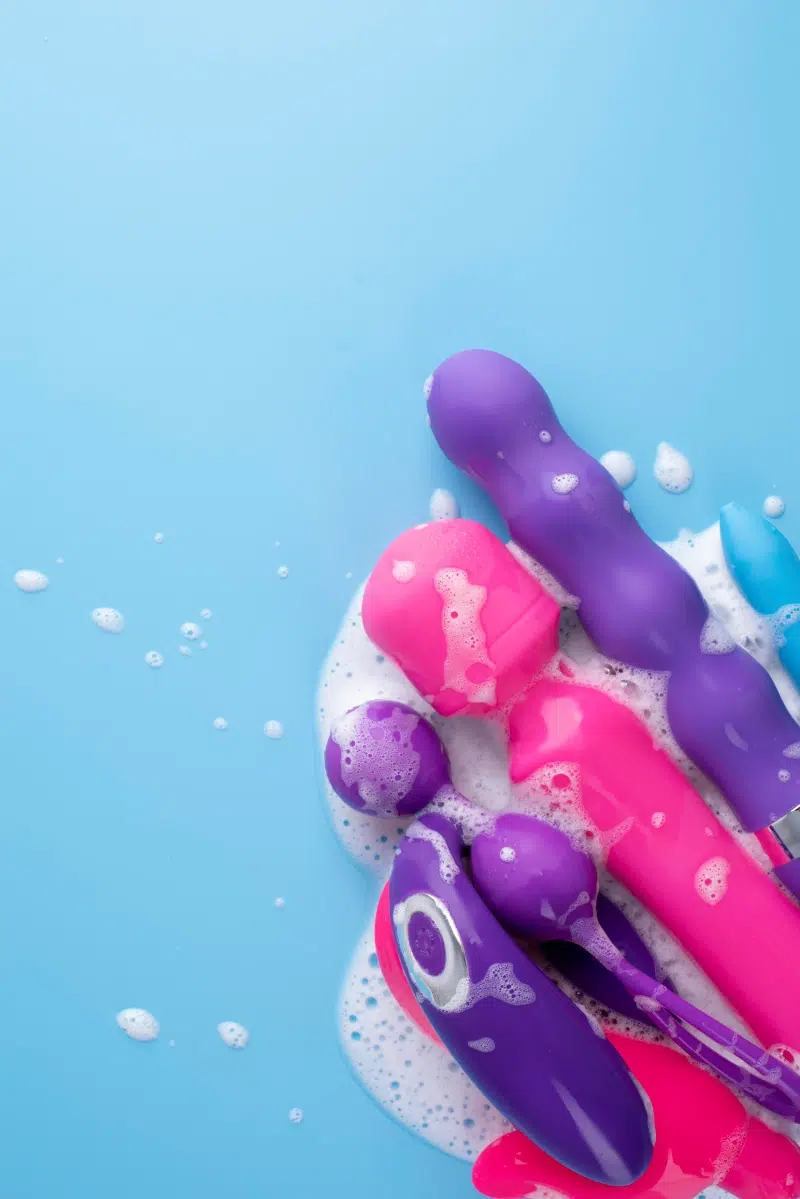 A variety of colorful waterproof vibrators and sex toys with foam on a blue background, showcasing their ability to handle water exposure.