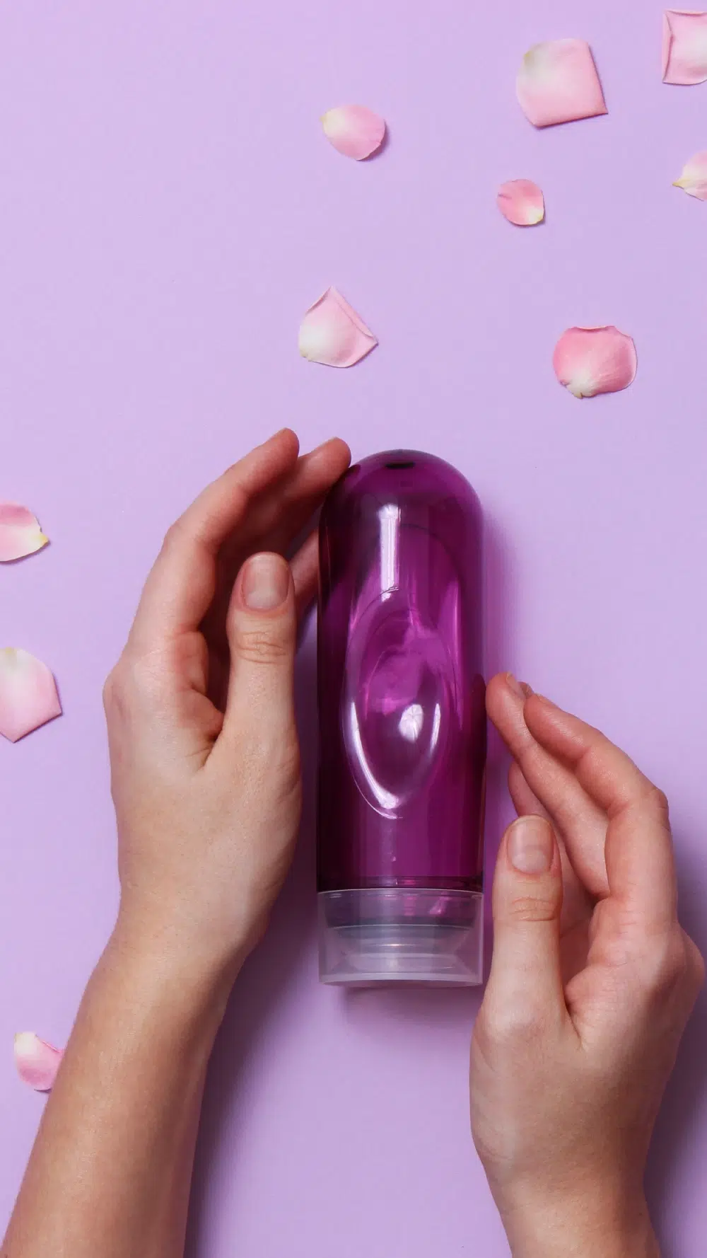Top view of hands presenting a purple masturbation sleeve, styled with rose petals on a pastel background