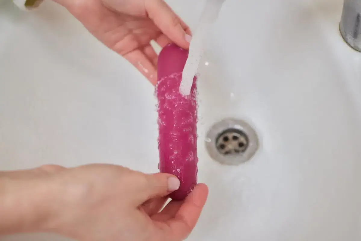 A person rinsing a waterproof vibrator under running water in a sink, demonstrating its ability to withstand water exposure.