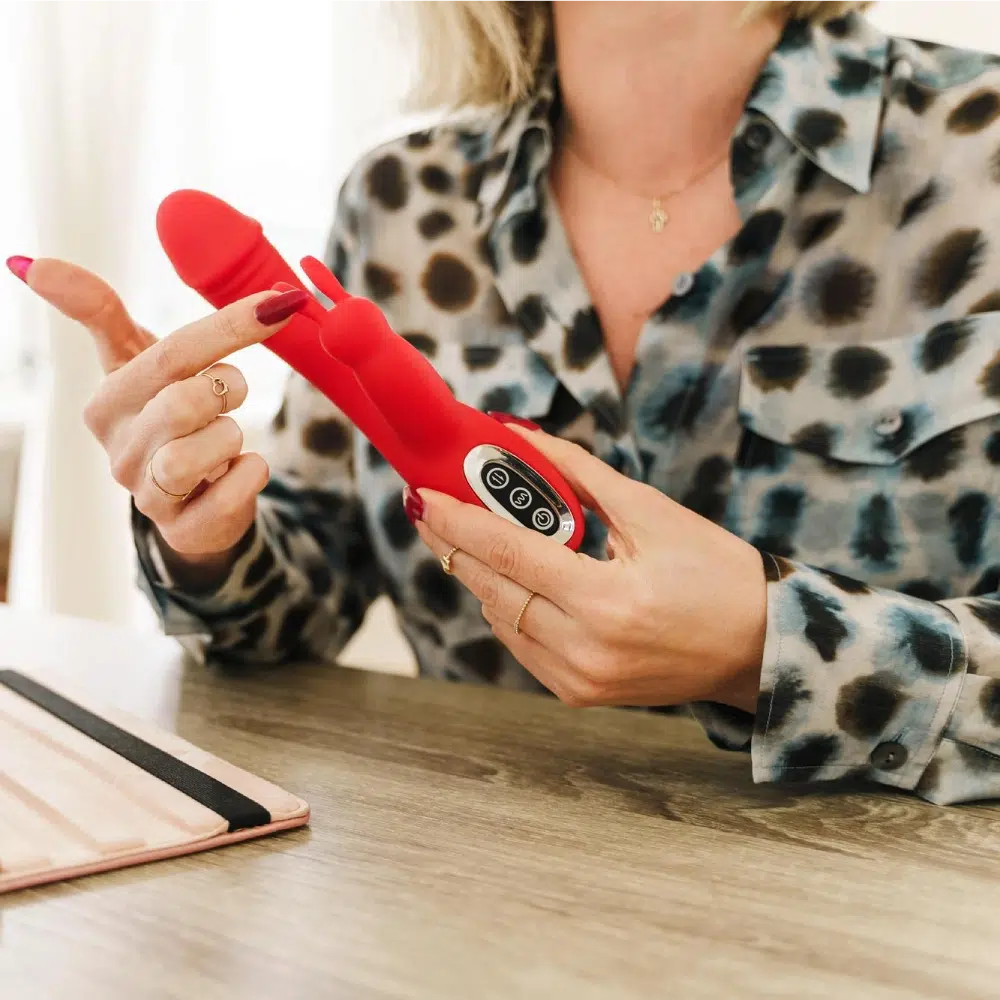 Woman holding a red rabbit vibrator and pointing at its control panel, highlighting design and button layout.