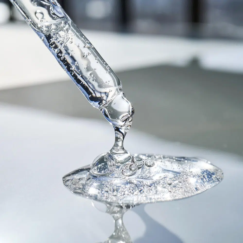 Clear gel dripping from a glass pipette onto a white surface.