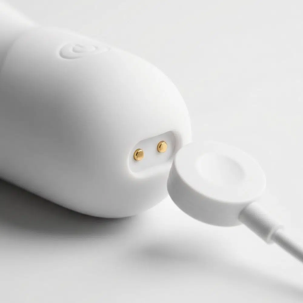 Close-up of a white vibrator’s magnetic charging port with two gold contact pins and a matching magnetic charger nearby.