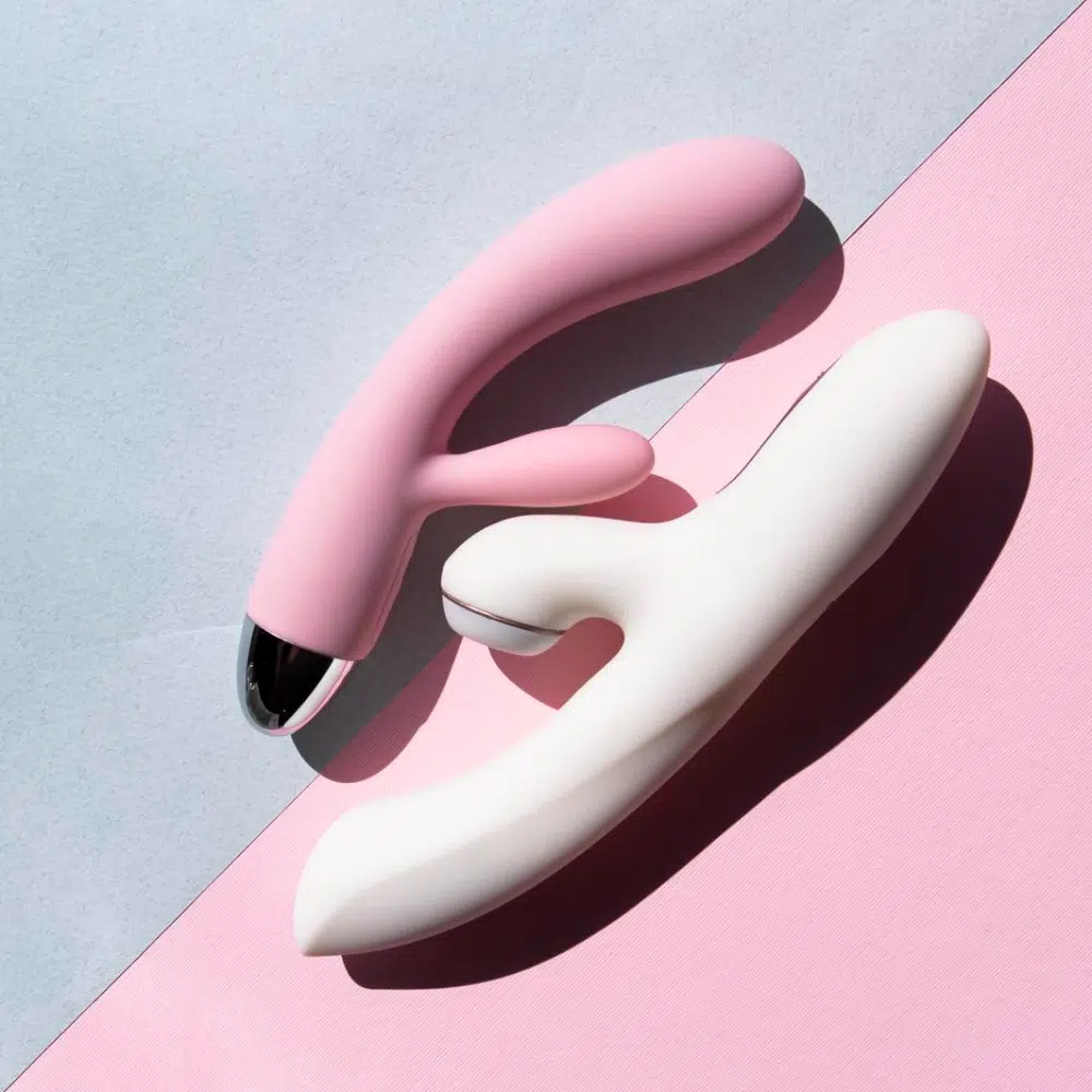 Two ergonomic vibrators in pink and white on a pastel background, showing different shapes and curves.